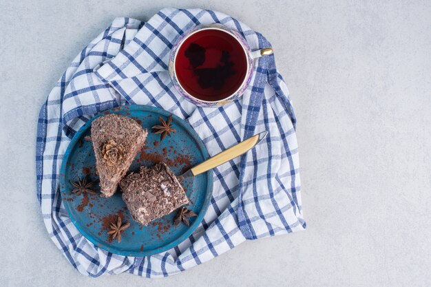 Cakes slices on a platter next to a cup of tea on marble table.