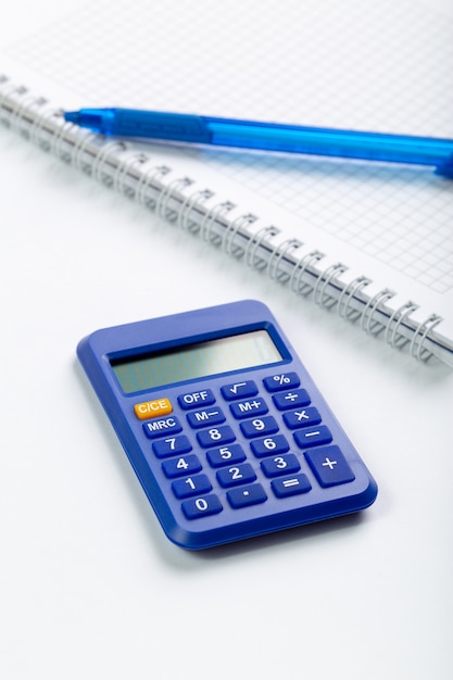Calculator blue accounting hand use for business matters along with copybook and pen on white desk