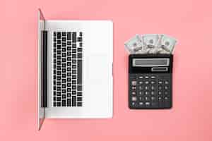 Free photo calculator laptop and dollar bills on colored background flat lay