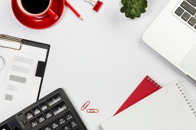 Calculator,laptop,spiral notepad,coffee cup,cactus plant on white desk