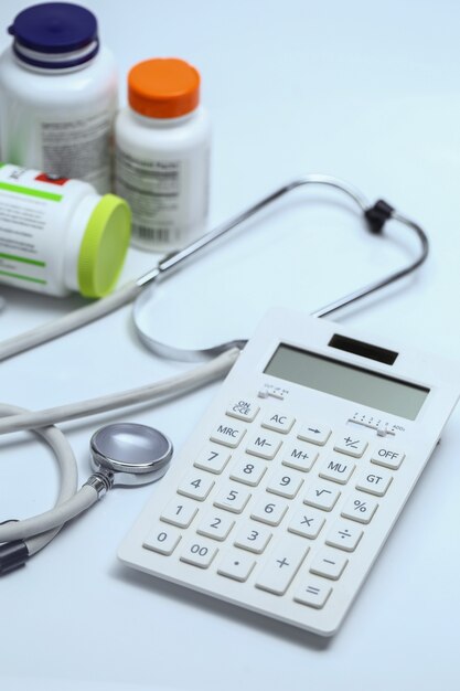 calculator, stethoscope and medicine bottles on white background