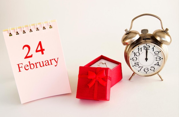 반지와 알람 시계가 있는 빨간색 선물 상자가 있는 밝은 배경의 달력 날짜 2월 24일