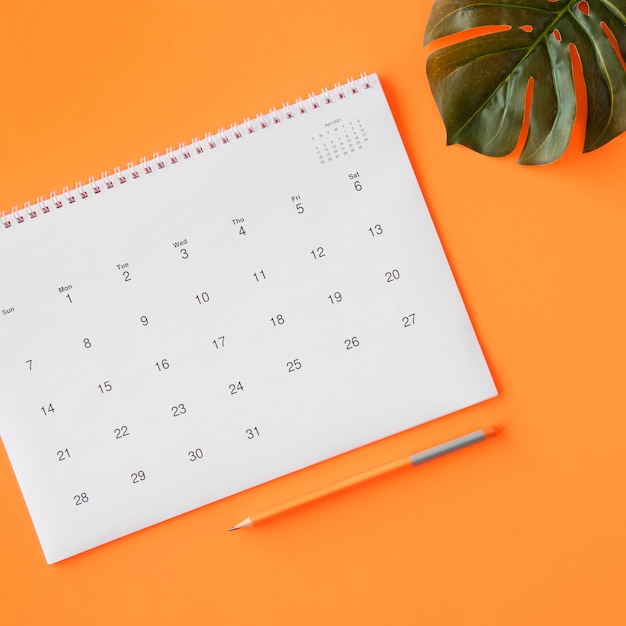 Free photo calendar with pencil and monstera leaf