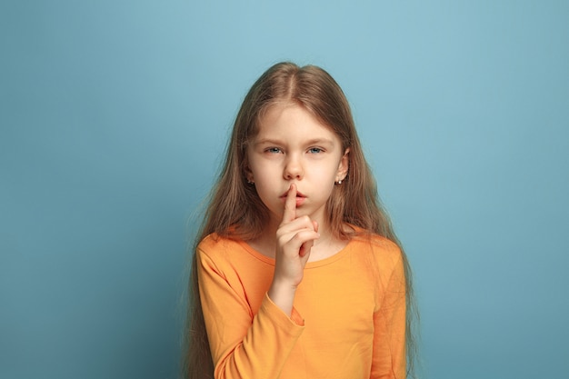 call for silence. surprised teen girl on a blue studio background. Facial expressions and people emotions concept.