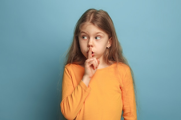 Free photo the call for silence. the surprised teen girl on a blue studio.