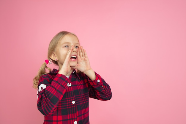 Calling, shouting. Caucasian little girl's portrait on pink wall. Beautiful female model with blonde hair. Concept of human emotions, facial expression, sales, ad, youth, childhood.