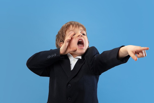 Calling, shouting. Portrait of a young orthodox jewish boy isolated on blue wall. Purim, business, festival, holiday, childhood, celebration Pesach or Passover, judaism, religion concept.