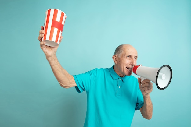 Calling with mouthpeace. Caucasian senior man's portrait on blue studio background. Beautiful male emotional model. Concept of human emotions, facial expression, sales, wellbeing, ad. Copyspace.