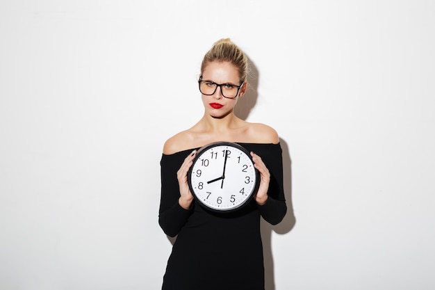 Бесплатное фото Спокойная деловая женщина в платье и очки, держа часы