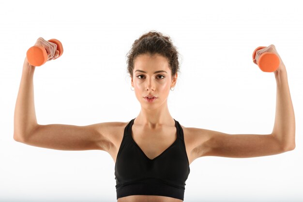 Calm curly brunette fitness woman doing exercise with dumbbells and showing her biceps