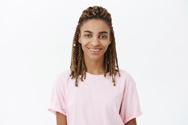 Foto gratuita calma e amichevole bella giovane femmina afroamericana con i dreadlocks in maglietta elegante rosa sorridente assicurato e gioioso