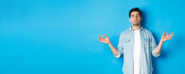 Calm man with closed eyes meditating holding hands sideways and do yoga breathing exercises standing