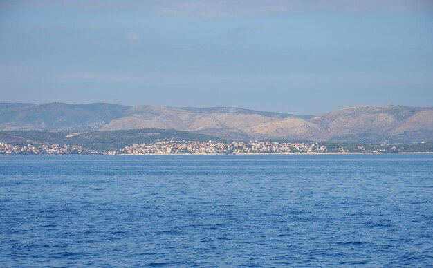 Calm ocean with glistening water and a coastal town and mountains in the horizon