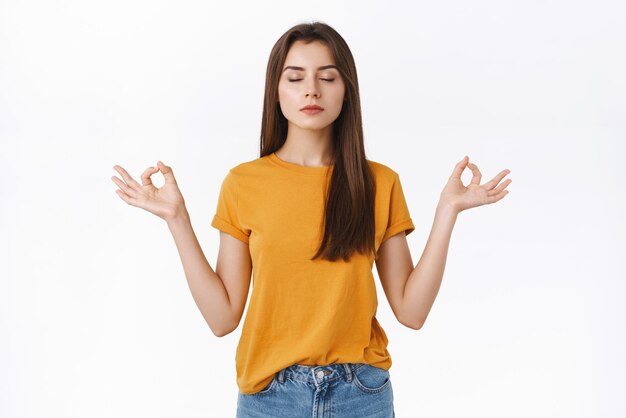 Calm patient and determined pretty young woman taking care own mind and soul close eyes while meditating with hands spread sideways in zen mudra sign reaching nirvana and peace white background