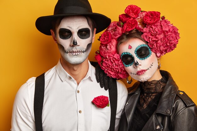 calm relaxed couple ready for popular carnival, apply spooky makeup, stand with eyes closed against yellow background.