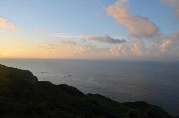 Calm sea surrounded by hills and greenery during sunset under a blue sky