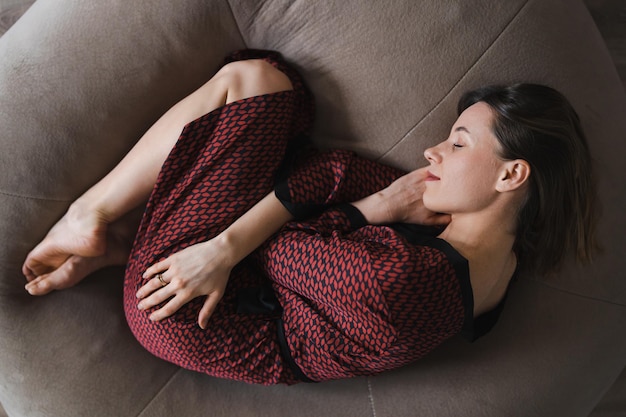 Calm serene beautiful young lady lying down in a dream relaxing sleep on a soft beige bean bag enjoying a good healthy sleep top view