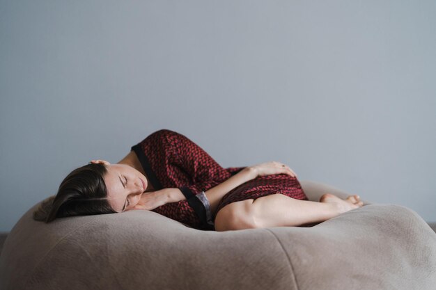 穏やかで穏やかな美しい若い女性が夢の中で横になって、健康的な睡眠を楽しんでいる柔らかいベージュのビーンバッグで眠りをリラックスさせます