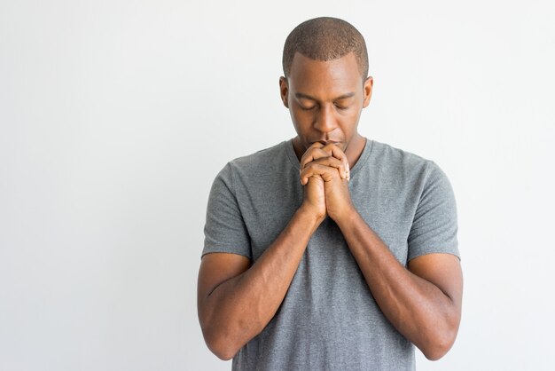Calm spiritual handsome african guy praying with closed eyes.