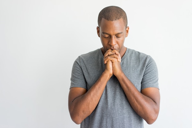 Calm spiritual handsome African guy praying with closed eyes.