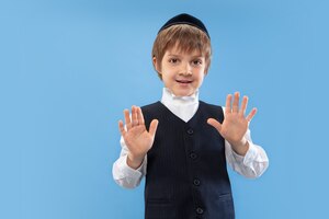 Бесплатное фото Успокойся, стой. портрет молодого православного еврейского мальчика, изолированного на синей стене. пурим, бизнес, фестиваль, праздник, детство, празднование песаха или пасхи, иудаизм, концепция религии.