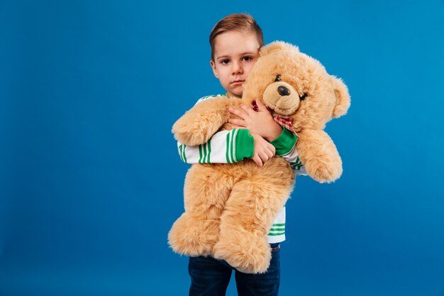 Calm young boy hugging teddy bear and looking