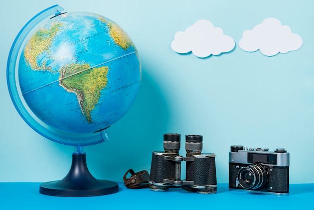 Camera and binoculars near globe and clouds