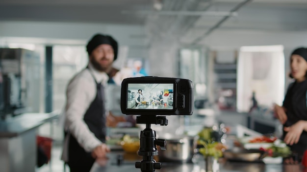 Camera filming people cooking professional menu dish in kitchen, recording online vlog for gastronomy show program on TV. Team of cooks teaching gourmet meal preparations. Tripod shot.