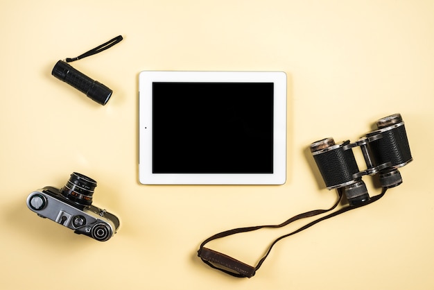 камера; фонарик; бинокль и цифровой планшет на бежевом фоне