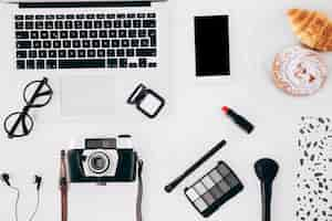 Free photo camera; laptop; mobilephone; cosmetics product and baked pastry on white desk