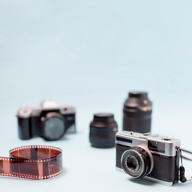 Camera; optical lens and rolled up film stripe on blue background