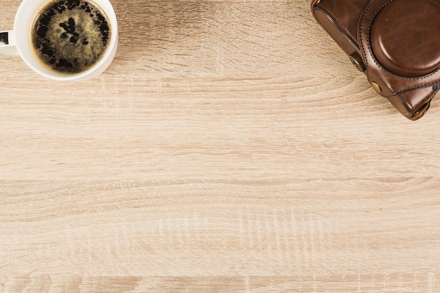 Camera in pouch and coffee cup on wooden table