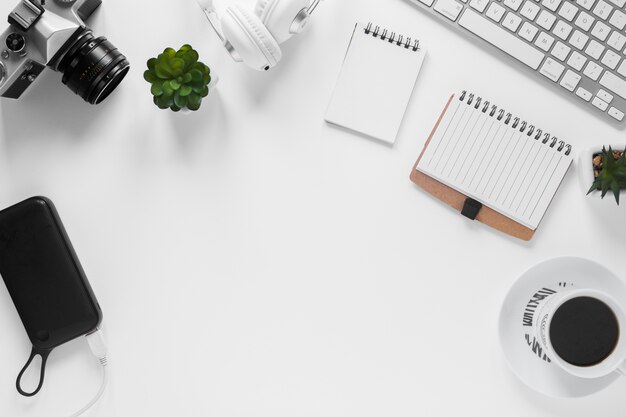 Camera; power bank; cactus plant; diary; tea cup and keyboard on white desk