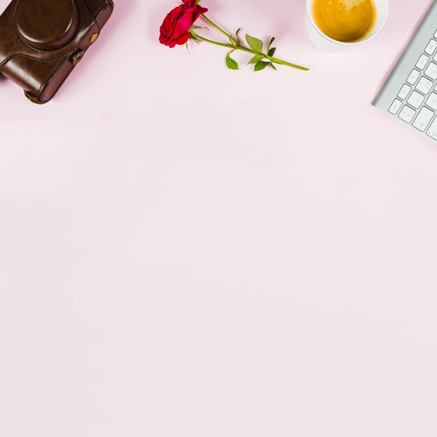 Camera; rose; tea cup and keyboard on pink background