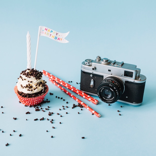 Камера и солома возле булочки с днем ​​рождения