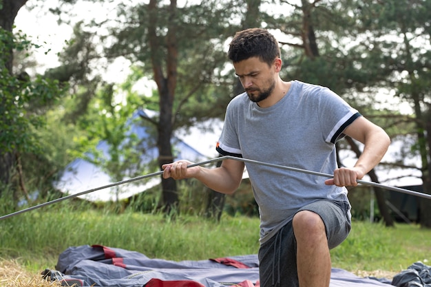 Camping, travel, tourism, hike concept - young man setting up tent outdoors.