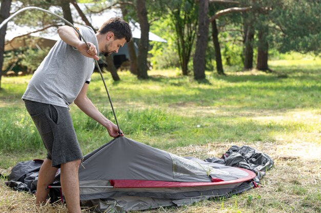 キャンプ、旅行、観光、ハイキングのコンセプト-若い男が屋外でテントを張る。