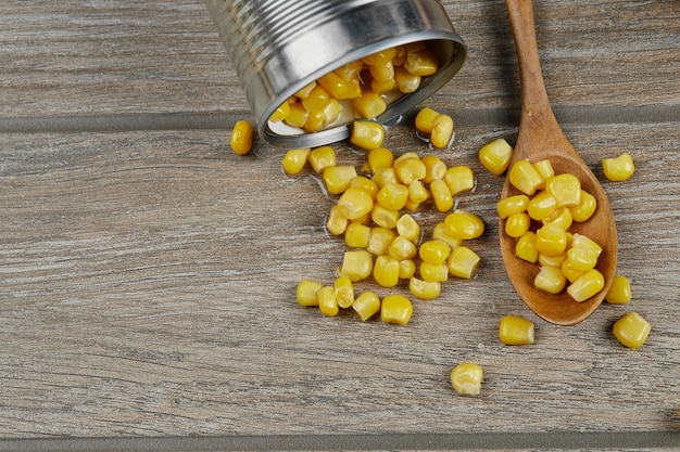 A can of boiled sweet corn on a wooden table with a spoon.