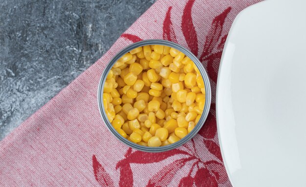 A can full of popcorn seeds with empty plate on tablecloth .