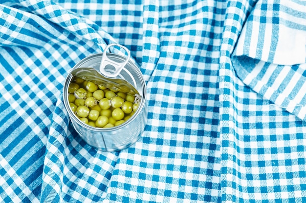 A can with boiled green peas on a blue tablecloth.