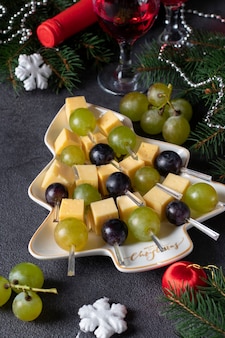 Canapes with cheese and grapes served in plate as christmas tree, on dark gray background. new year's eve party snack Premium Photo