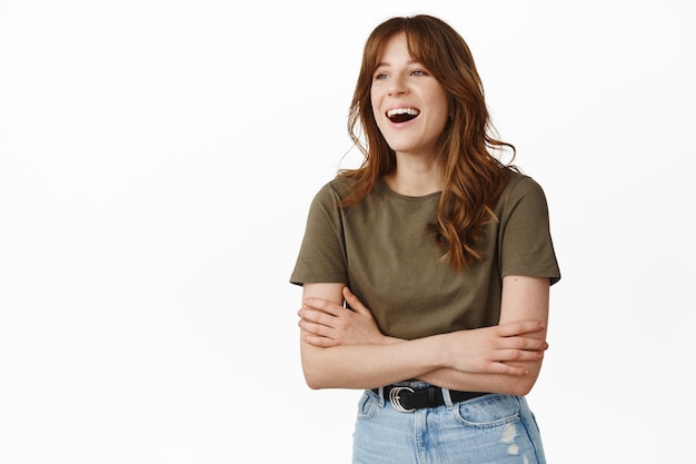 Candid girl laughing and talking to friend, cross arms on chest, looking aside at person, watching something funny, standing in t-shirt on white