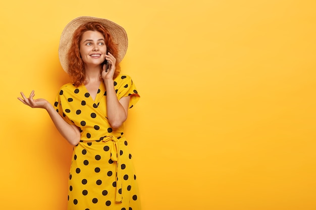 Candid redhead woman posing in yellow polka dress and straw hat