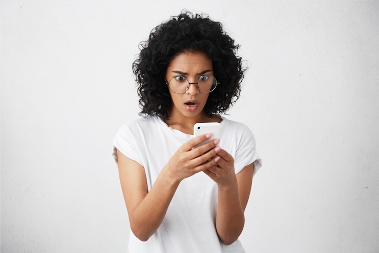Free Photo candid shot of amazed businesswoman with bushy curly hair dressed casually holding her smartphone