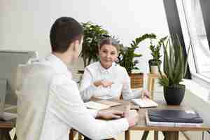 Free photo candid shot attractive confident middle aged female employer sitting at desk with copybook, making notes during job interview with prospective unrecognizable young male candidate. film effect