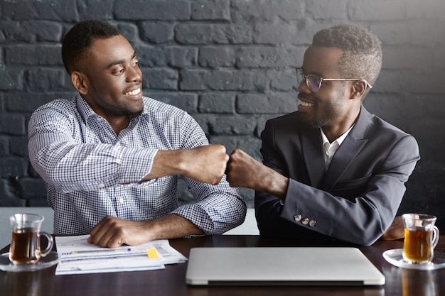 Free photo candid shot of happy successful dark-skinned businessmen wearing formal clothing fist-bumping