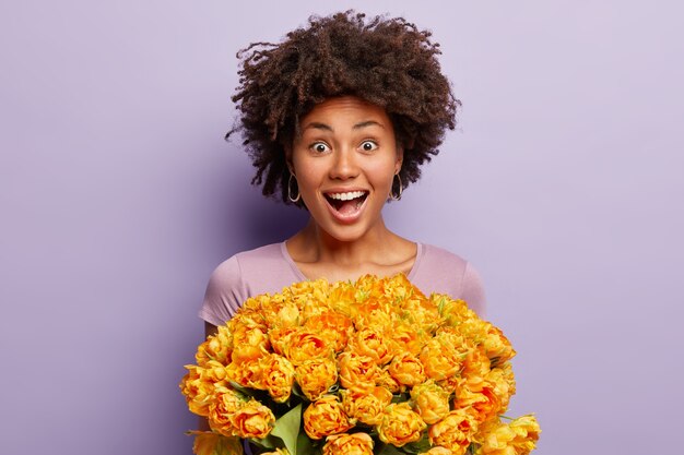 Candid shot of overemotive beautiful dark skinned female reacts positively at received tulips