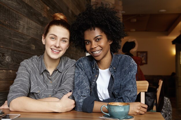 Candid shot of two happy lesbians spending nice time together, having coffee at cozy cafe