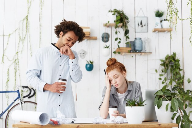 Candid shot of two tired and sleepy young man and woman architects facing deadline