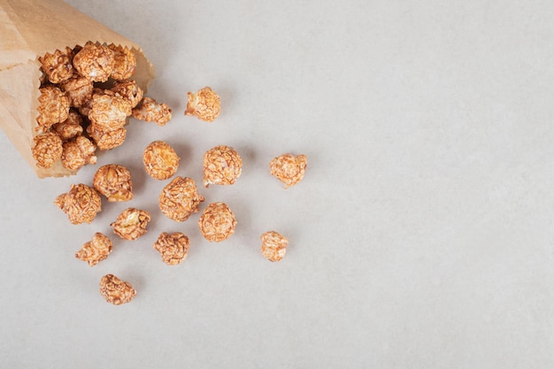 Candied popcorn spilling out of paper wrapping on marble background. 